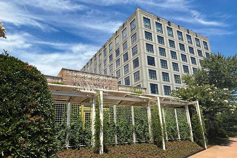 Print Works Bistro adjacent to Proximity Hotel Proximity Hotel and Print Works Bistro facade late summer 2025. Garden Trellis provides abundant shade and a cool place to have a cocktail with friends.